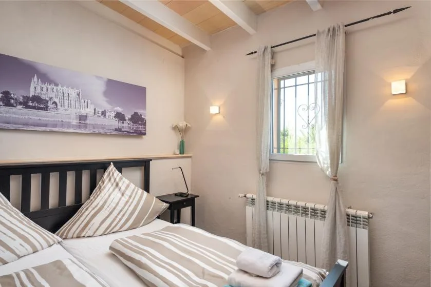 A bedroom with a bed, striped linens, and a window with sheer curtains.