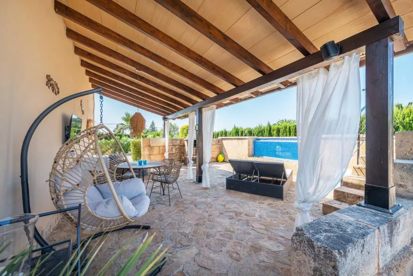 A covered outdoor patio has seating, a dining table, and a view of the pool.