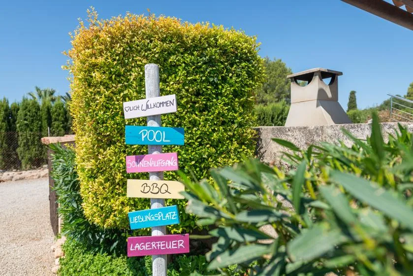 A leafy outdoor garden with a colorful signpost beside a barbecue area.