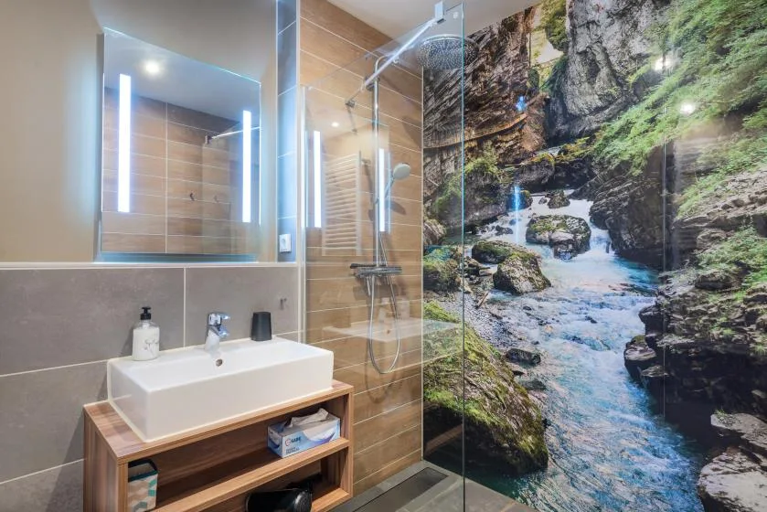 A modern bathroom with a sink, glass shower, and scenic nature mural.