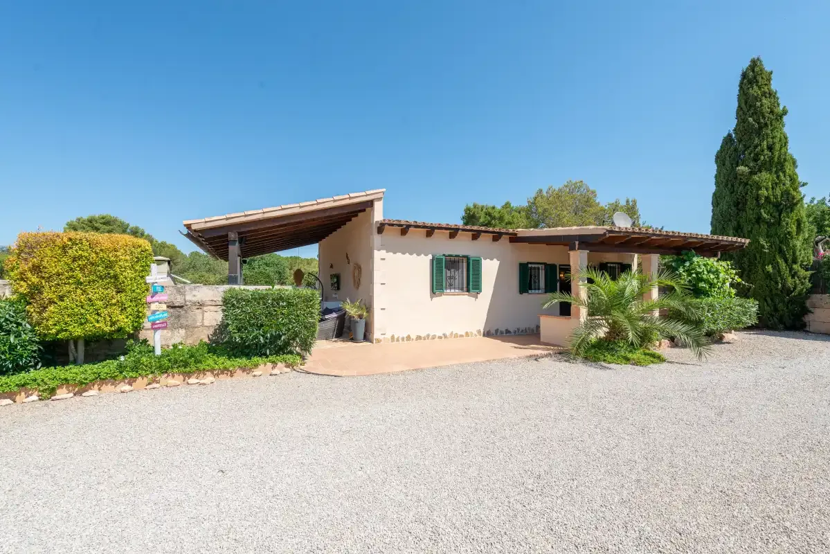 A low stucco building with a covered entrance stands beside a wide gravel driveway.