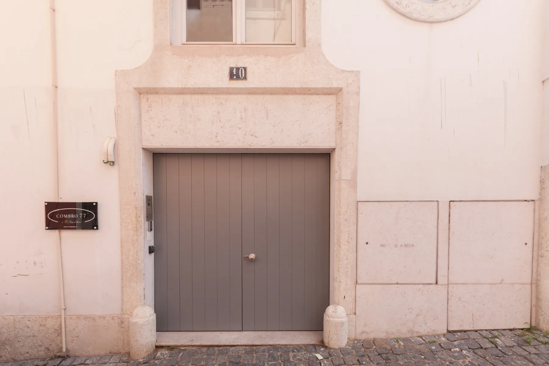 A gray garage door is set into a pale stone facade above a cobblestone street.