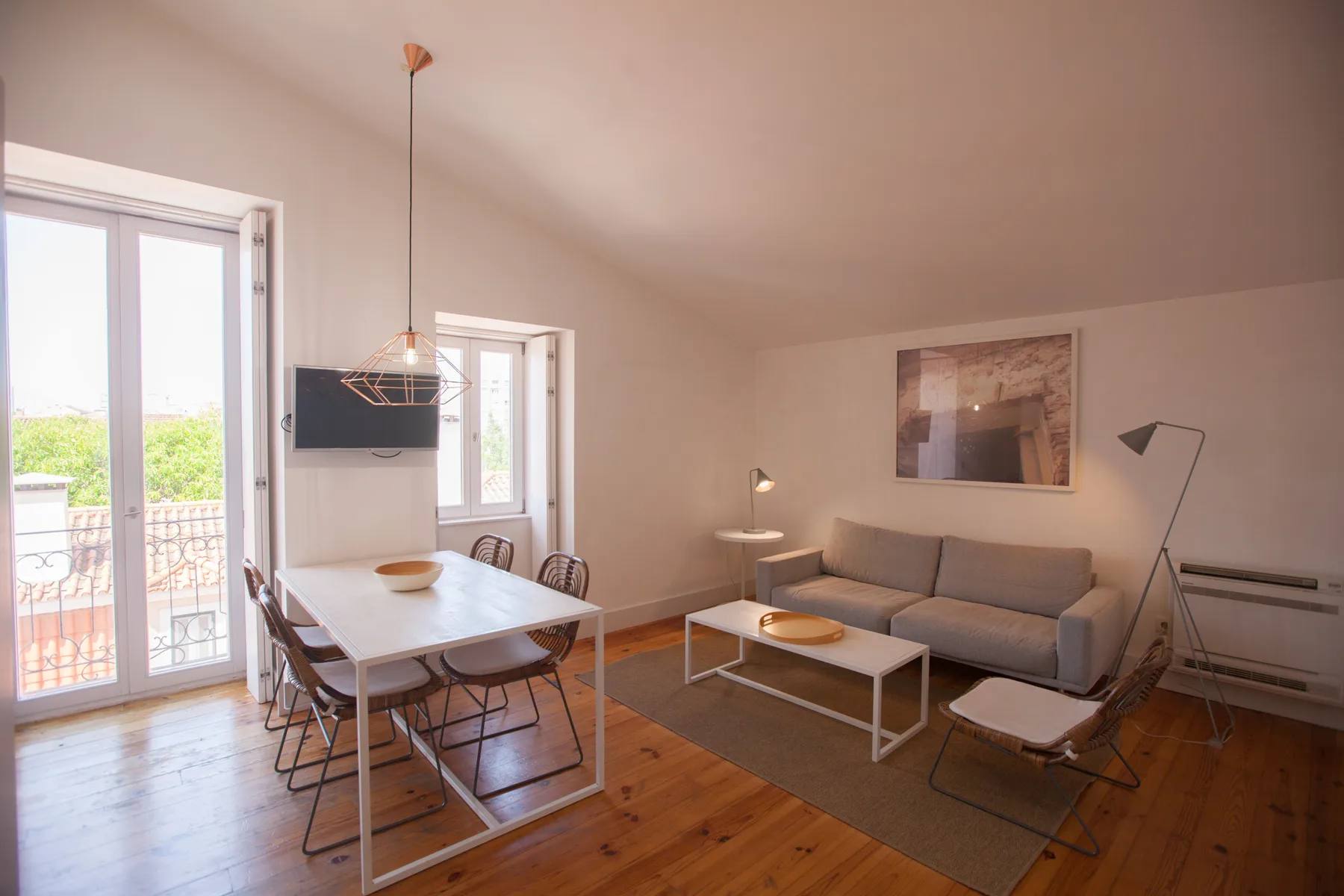 A bright living and dining area with a gray sofa and a table beside the windows.