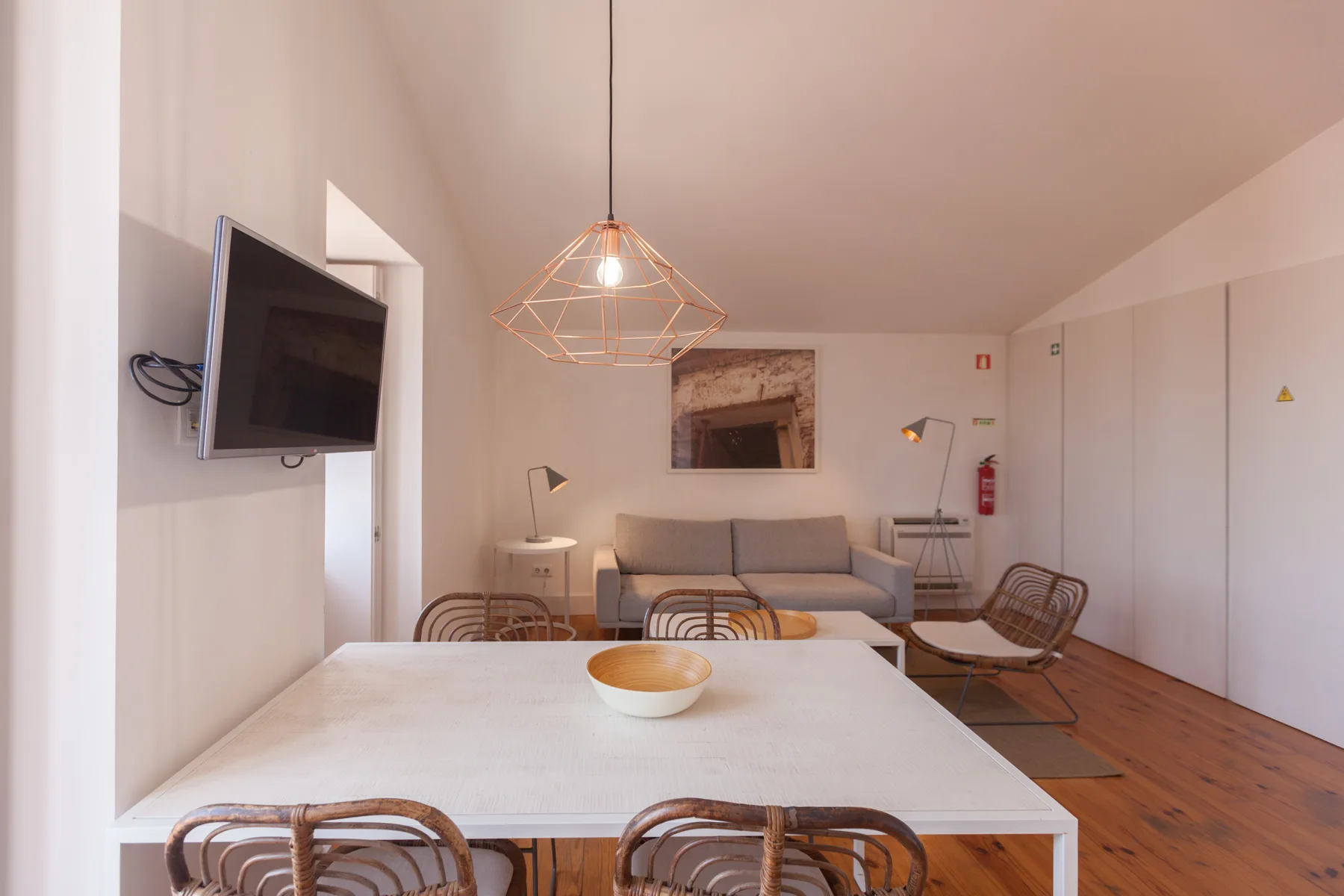 A dining and seating area with a white table, chairs, and a wall-mounted television.