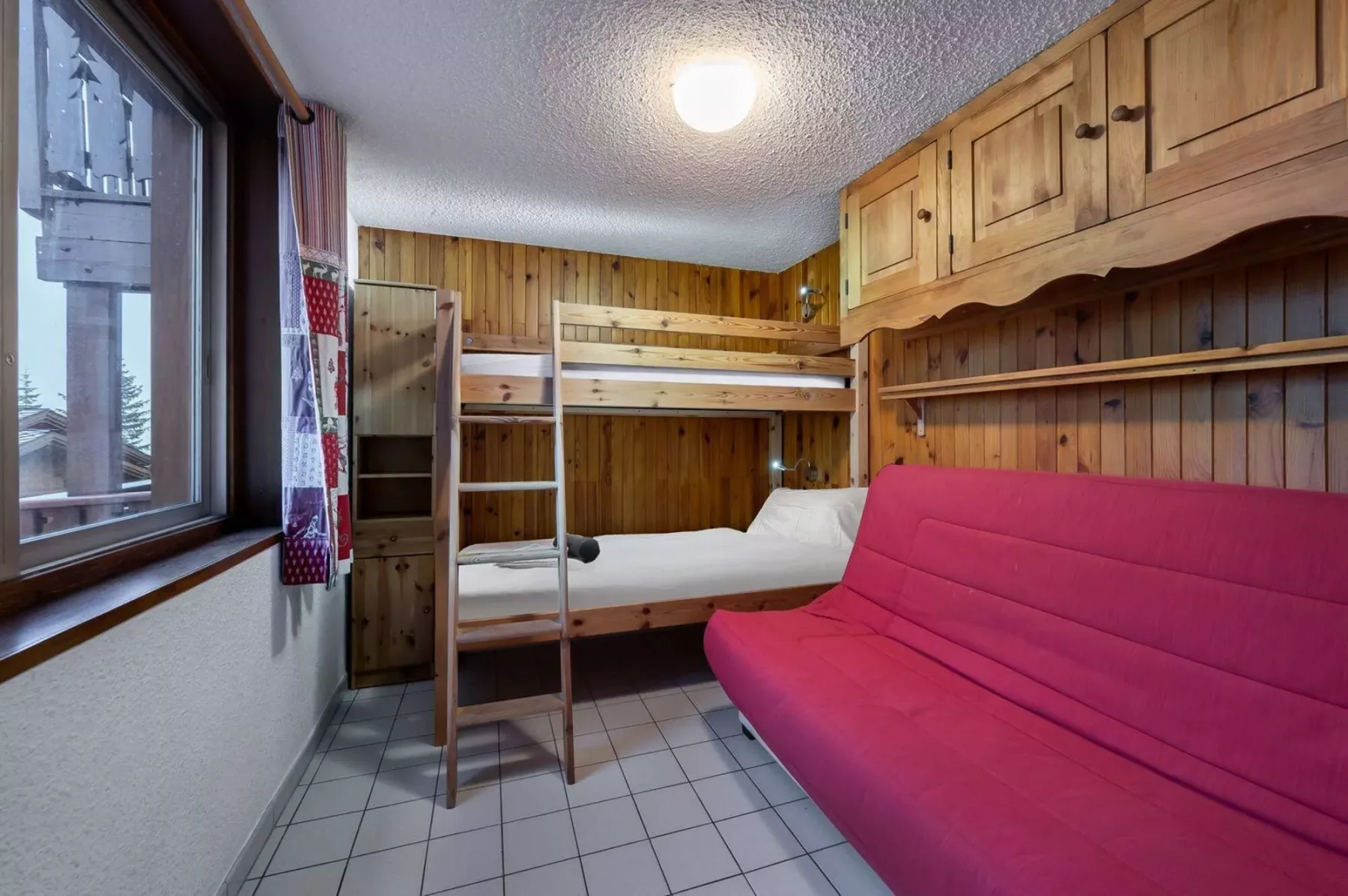 A wood-paneled room with bunk beds and a red sofa.