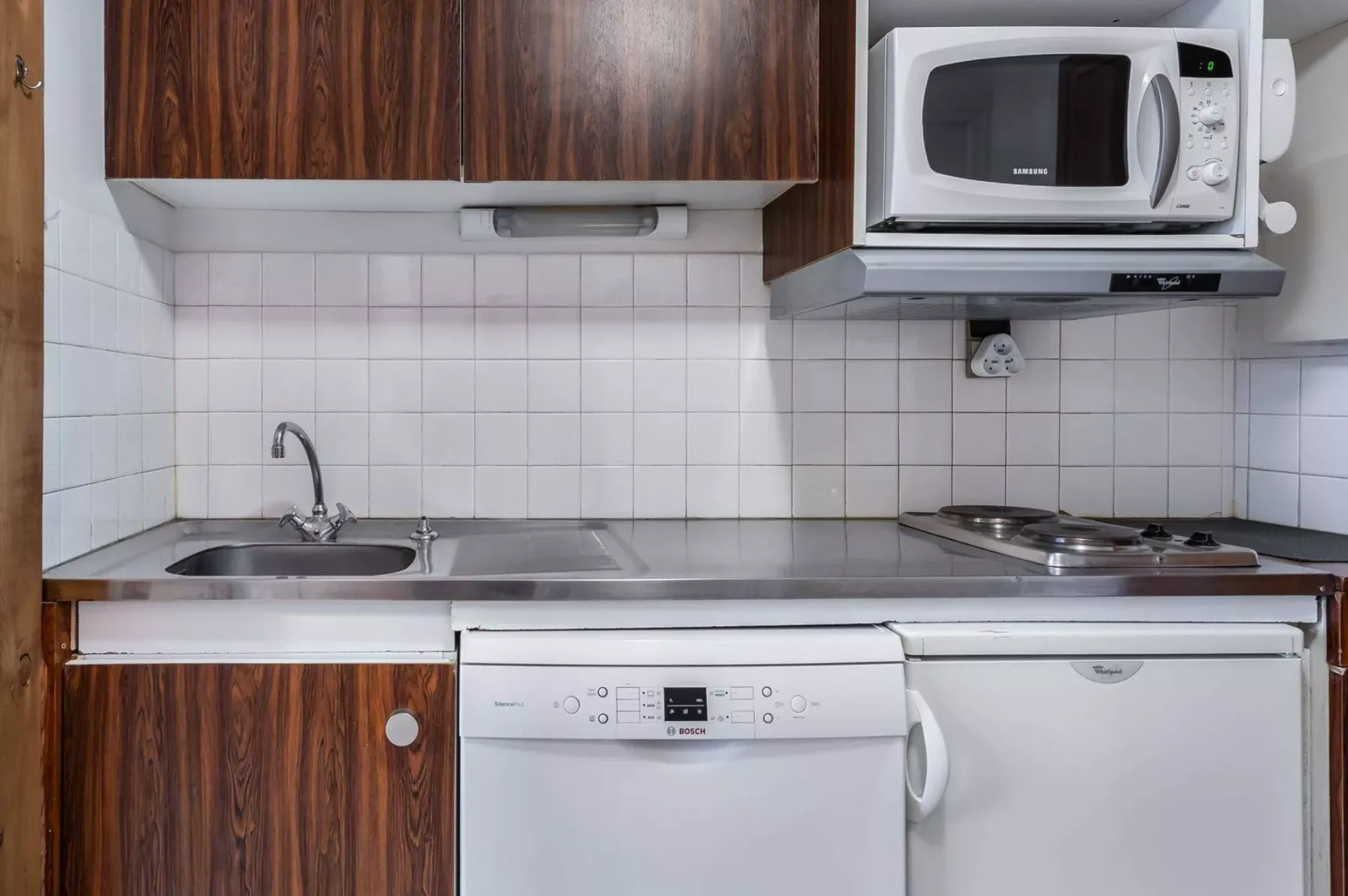 A compact kitchen with a sink, stovetop, microwave, and built-in appliances.
