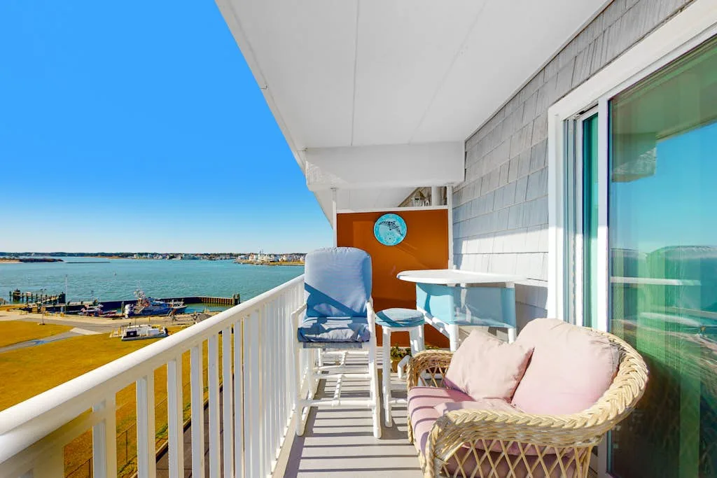 A balcony overlooking the water, with outdoor seating and a small table.