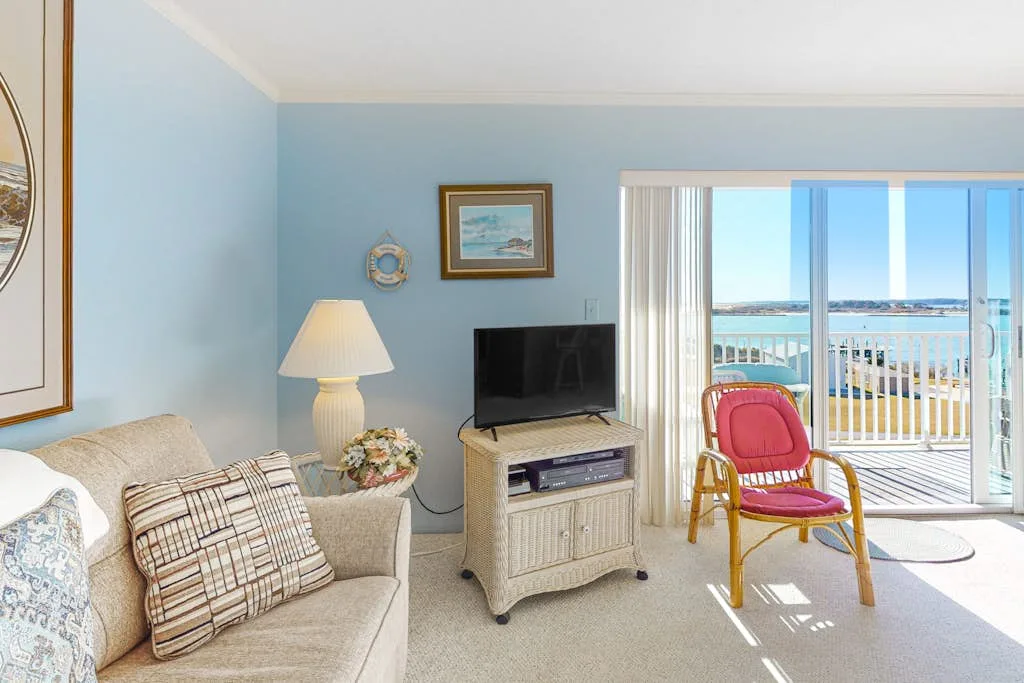 A living room with seating and a television beside sliding glass doors overlooking the water.