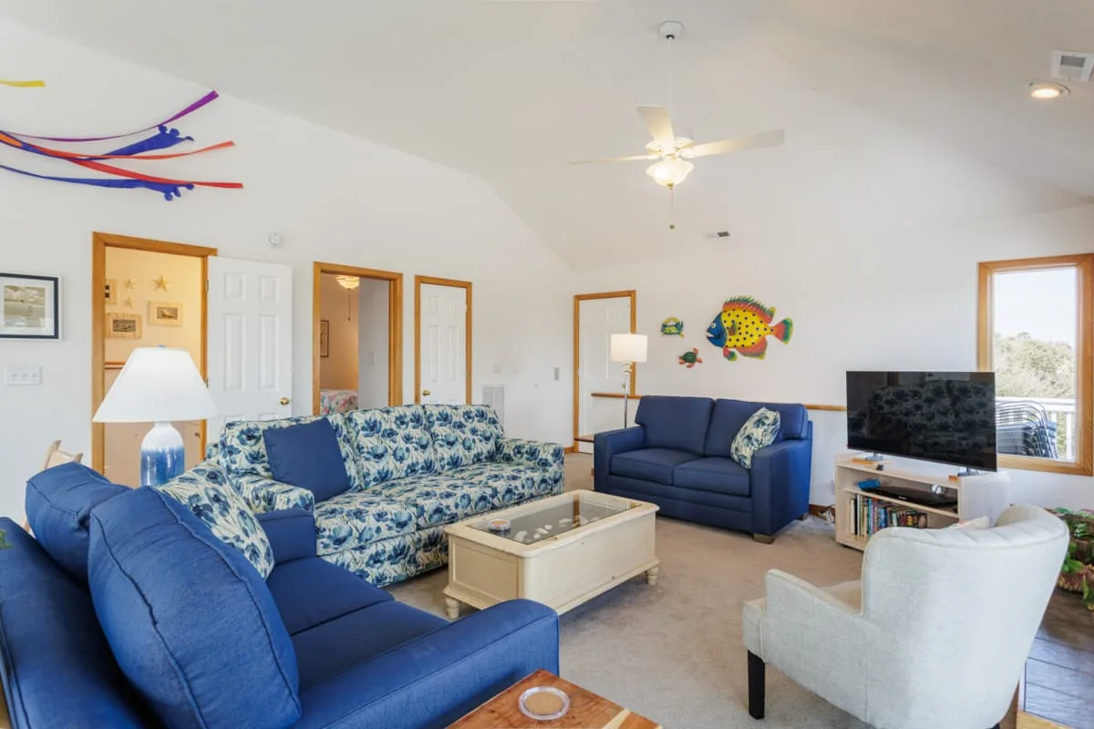 Una sala luminosa con asientos azules, una mesa de centro y un televisor.