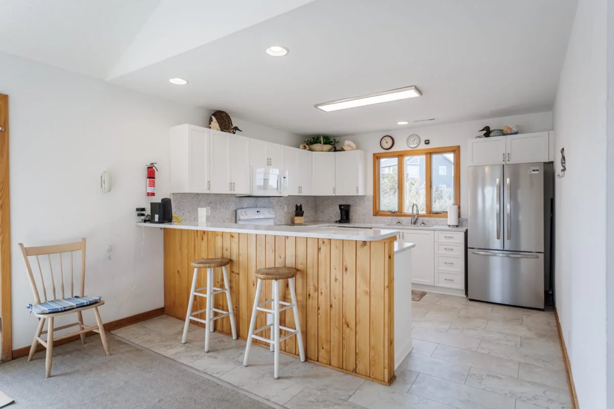 Una cocina luminosa con una isla de madera, gabinetes blancos y un refrigerador de acero inoxidable.