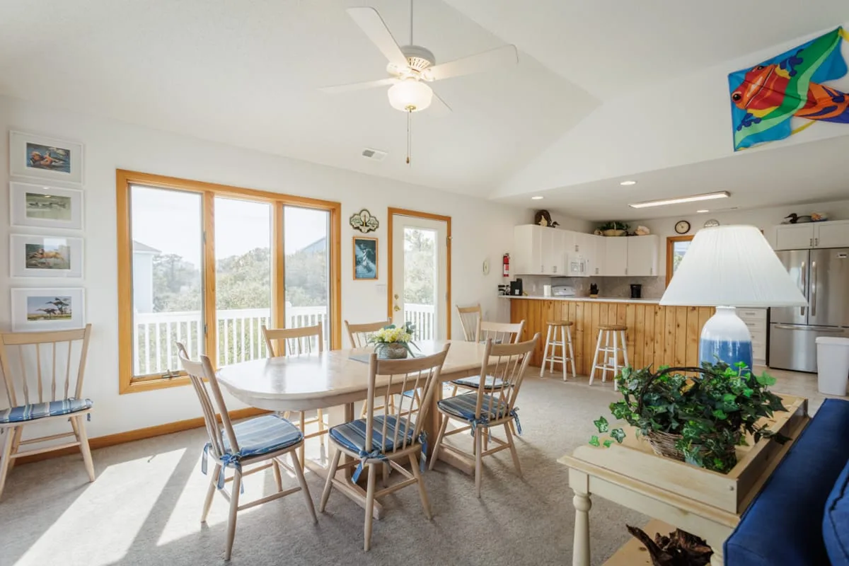 Comedor con una mesa de madera y sillas junto a grandes ventanas.