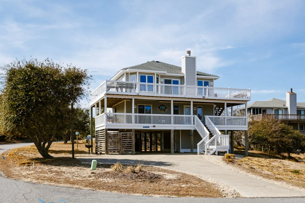 Una casa elevada tiene terrazas blancas alrededor y escaleras exteriores.