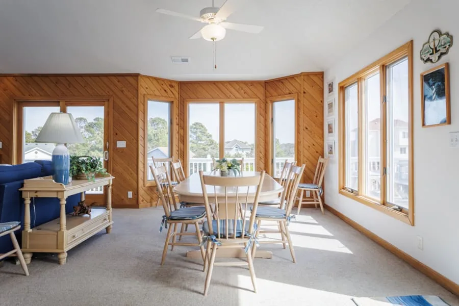 Una luminosa zona de comedor con una mesa de madera y sillas junto a grandes ventanas.