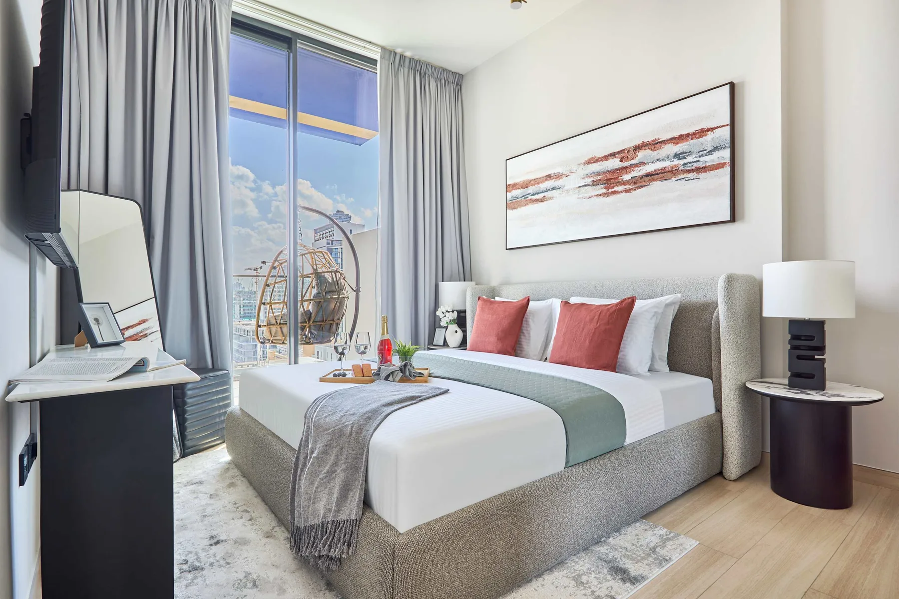 A bedroom with a neatly made bed, red accent pillows, and a large window.