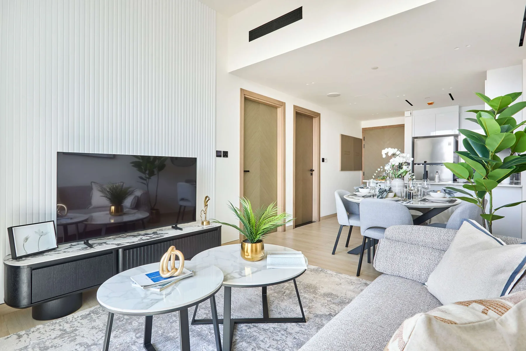 A bright living and dining area with seating, coffee tables, and a television.
