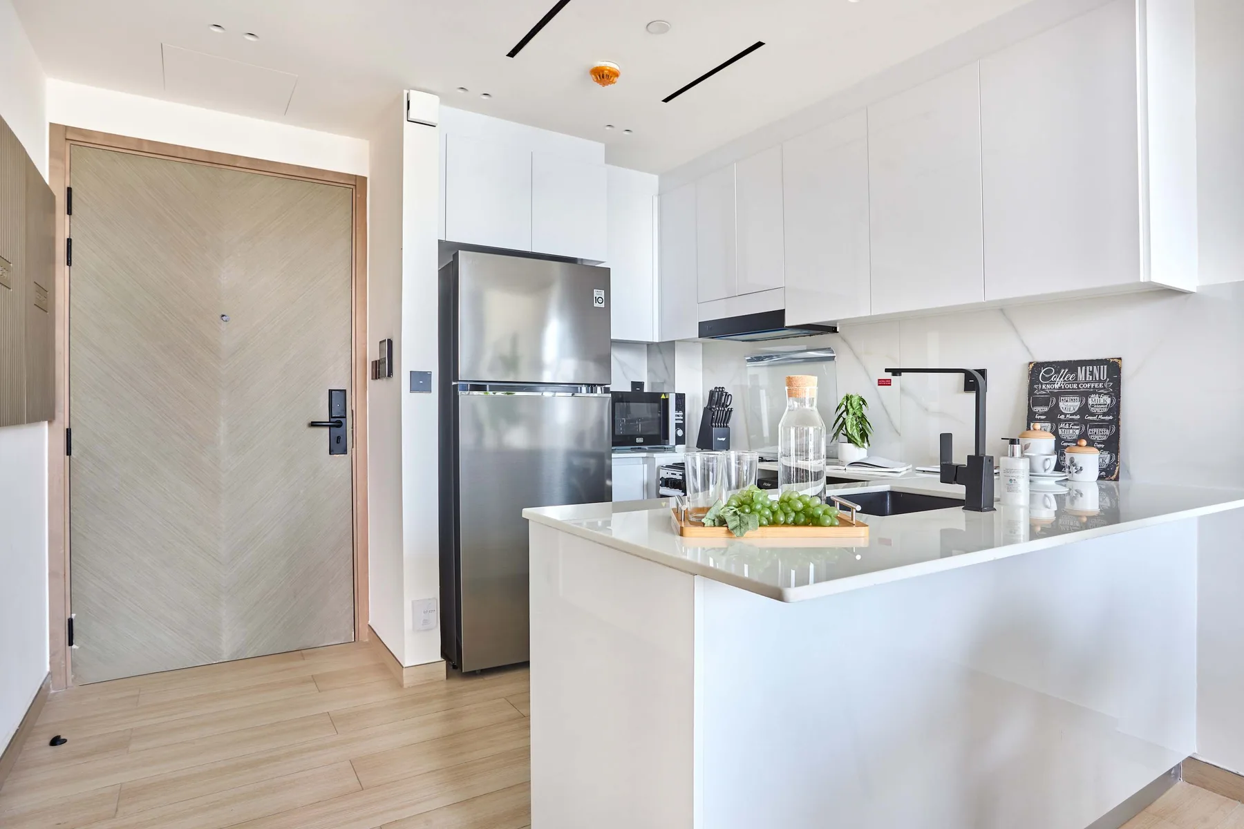 A bright modern kitchen with a central island and stainless steel refrigerator.