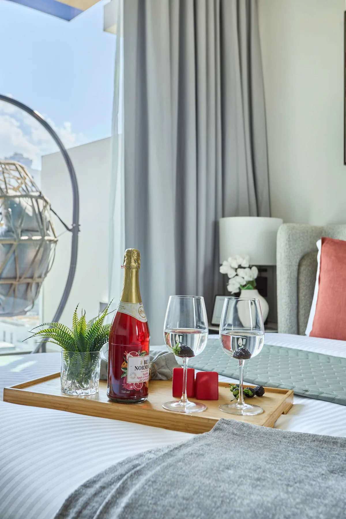 A bedroom scene with a tray of drinks on the bed beside a window.