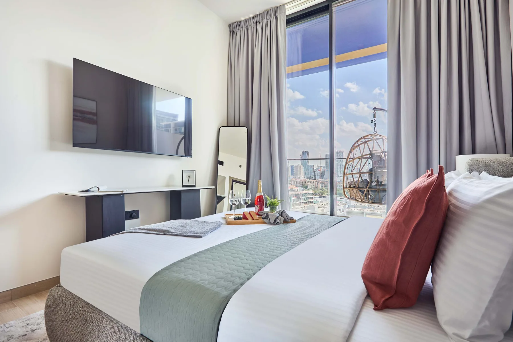 A bedroom with a neatly made bed, wall-mounted television, and large curtained window.