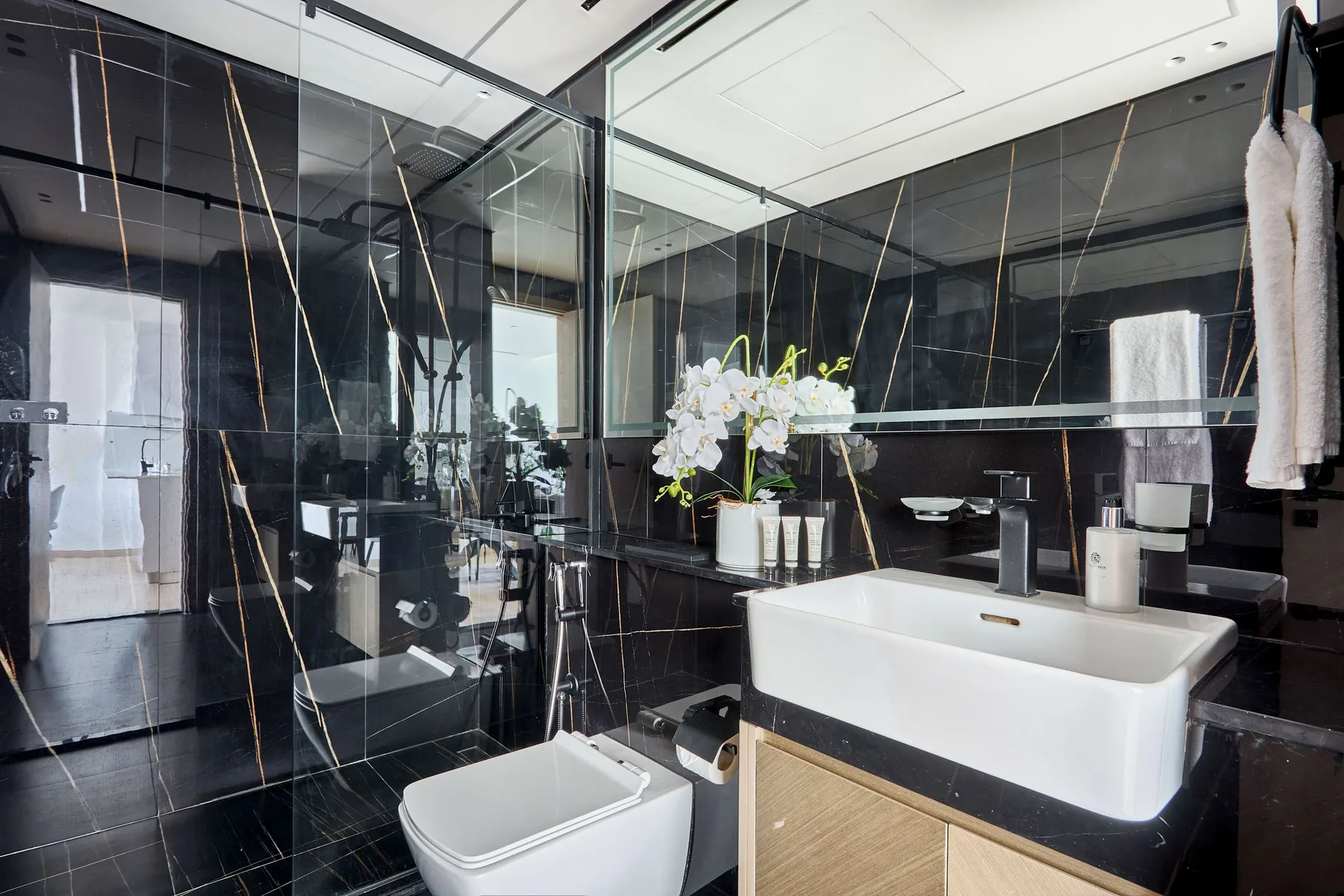 A modern bathroom with dark tiled walls, a glass shower, and a freestanding bathtub.