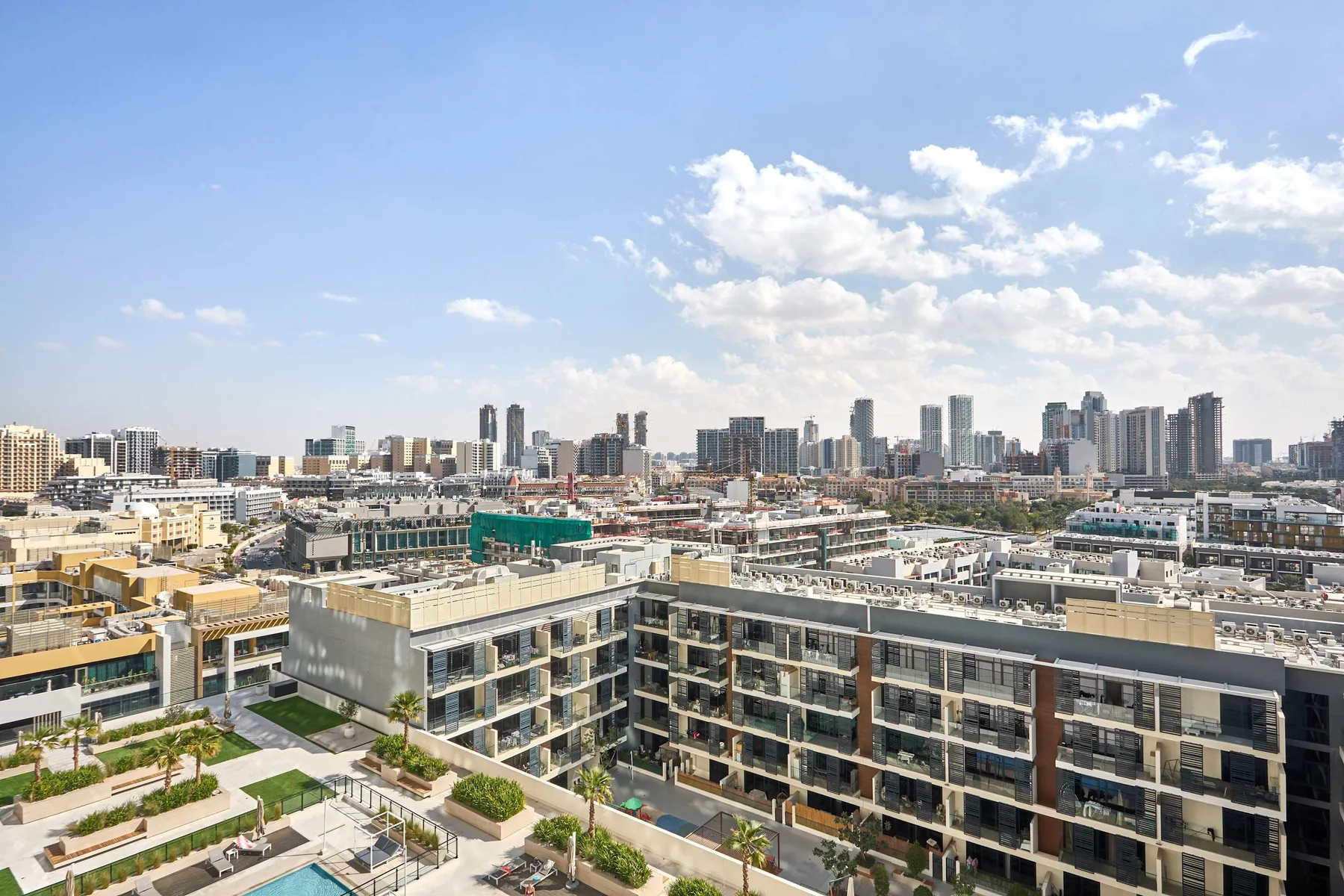 A city skyline rises behind modern buildings and a landscaped pool area.