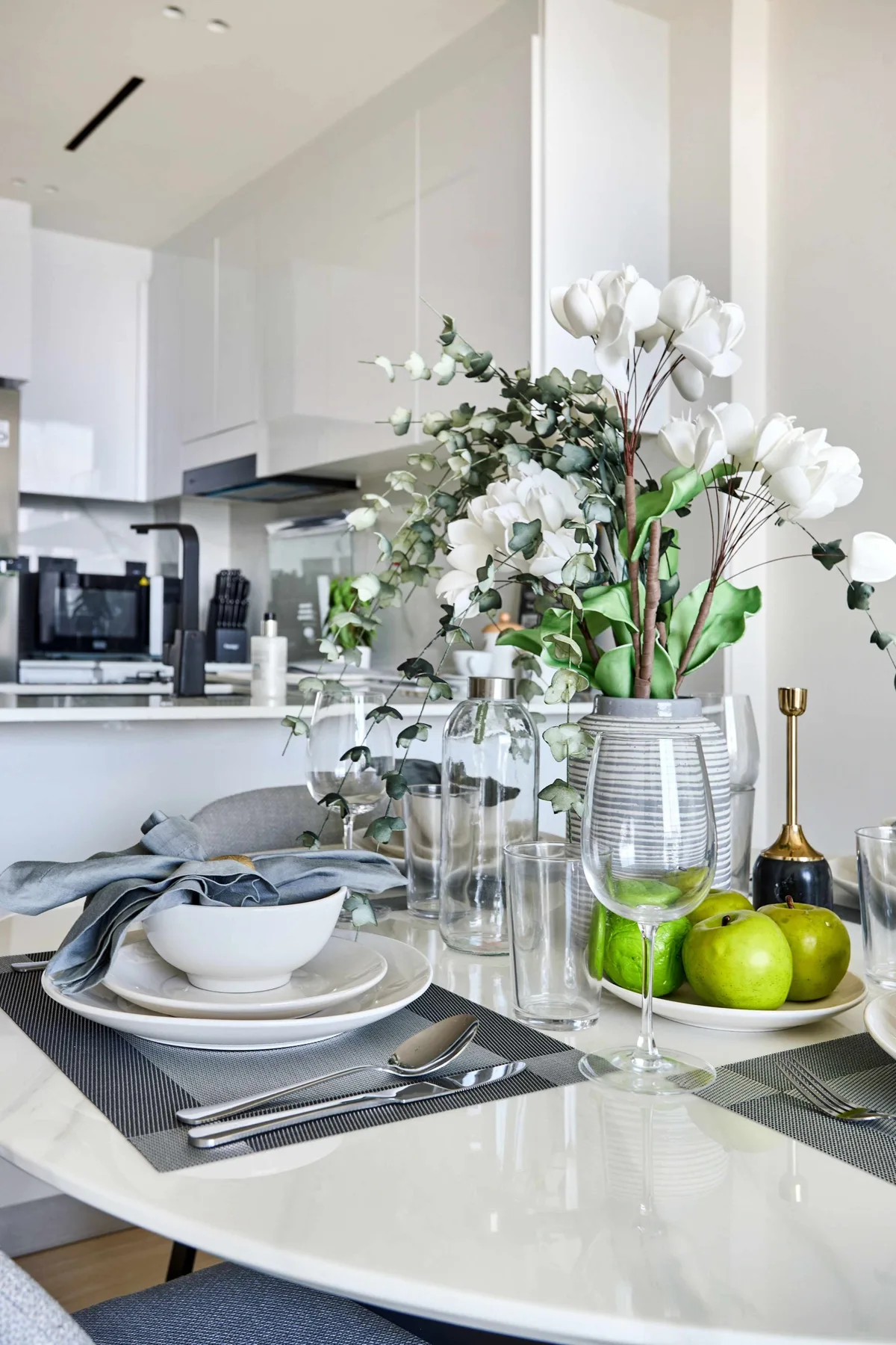 A bright dining table is set with dishes, glassware, green apples, and flowers.