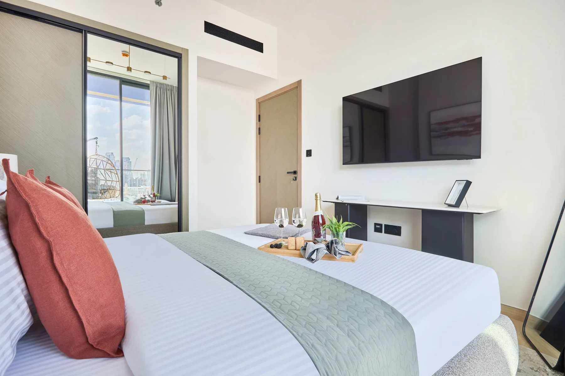 A bedroom with a bed, wall-mounted television, and glass doors opening to a balcony.