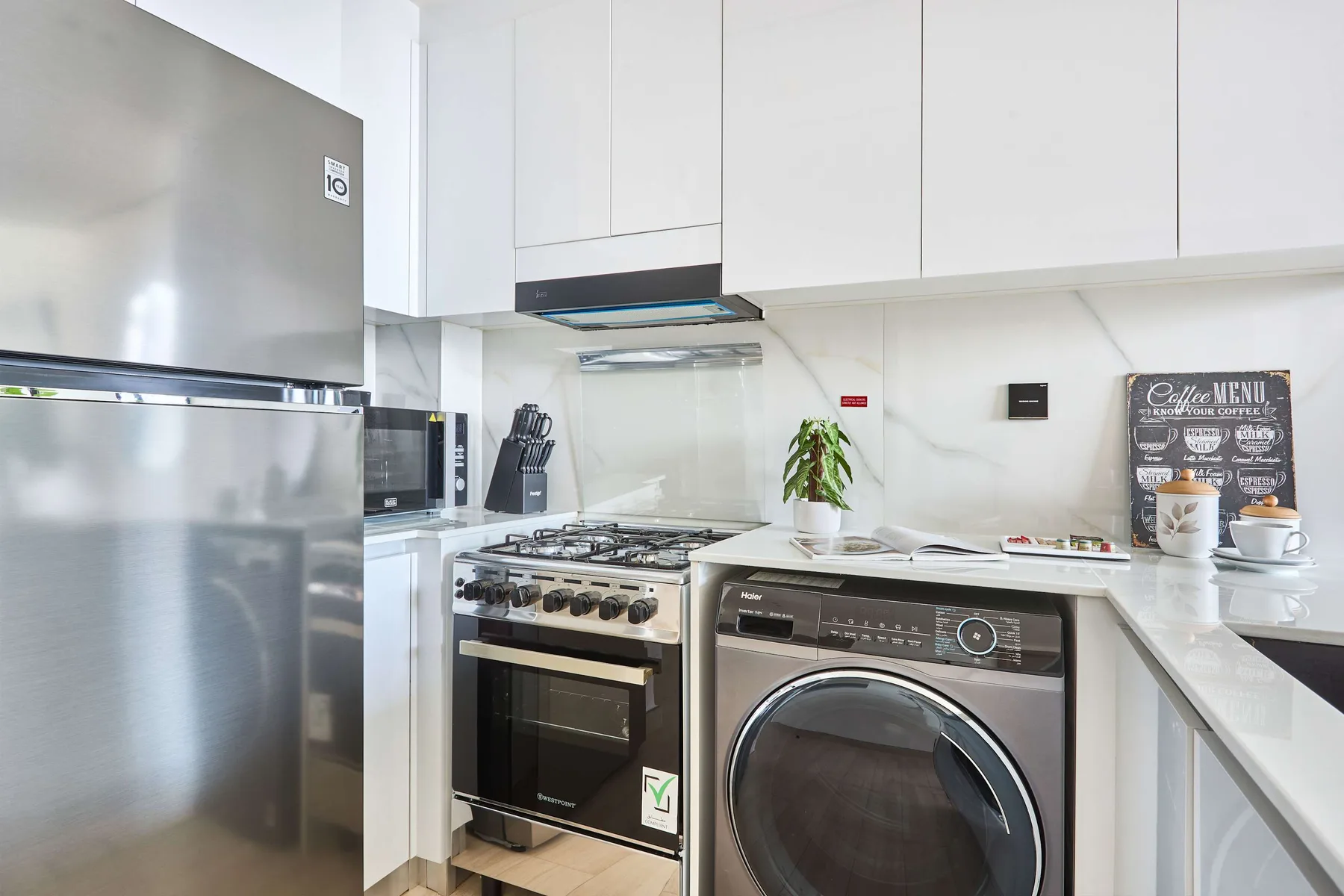 A bright kitchen with a stainless-steel refrigerator, stove, and front-loading washer.