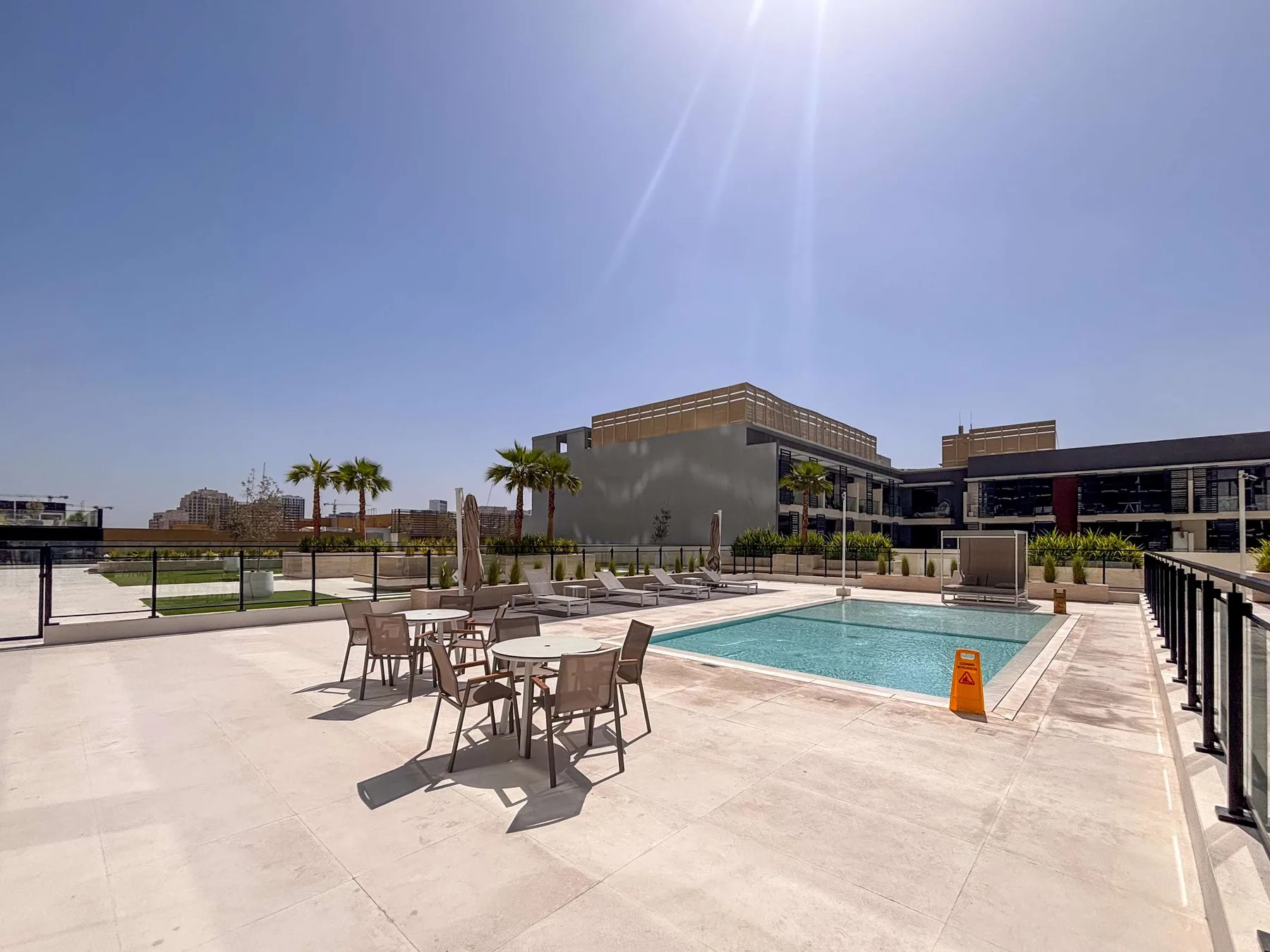 An outdoor pool area has seating and palm trees beside modern buildings.