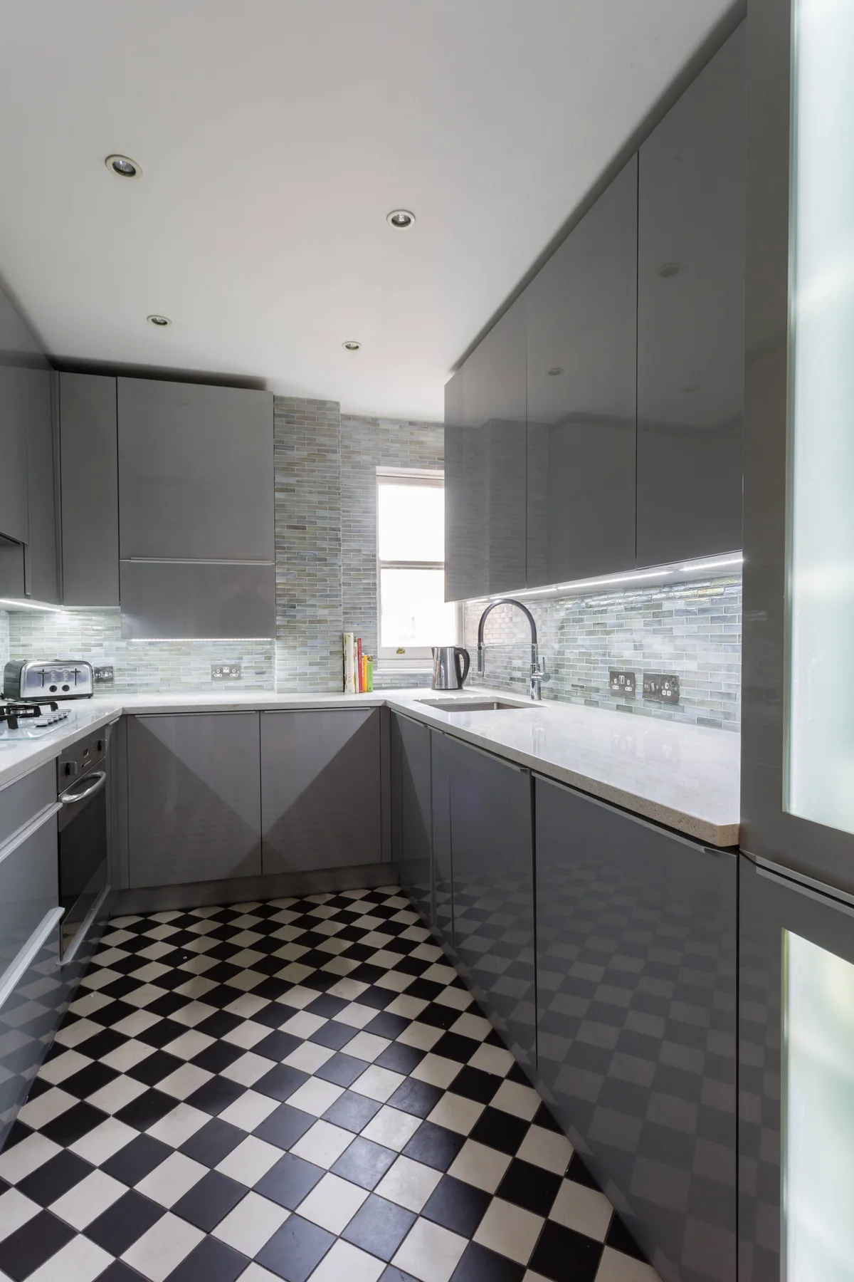 A modern kitchen with gray cabinets, a countertop, and a checkered floor.