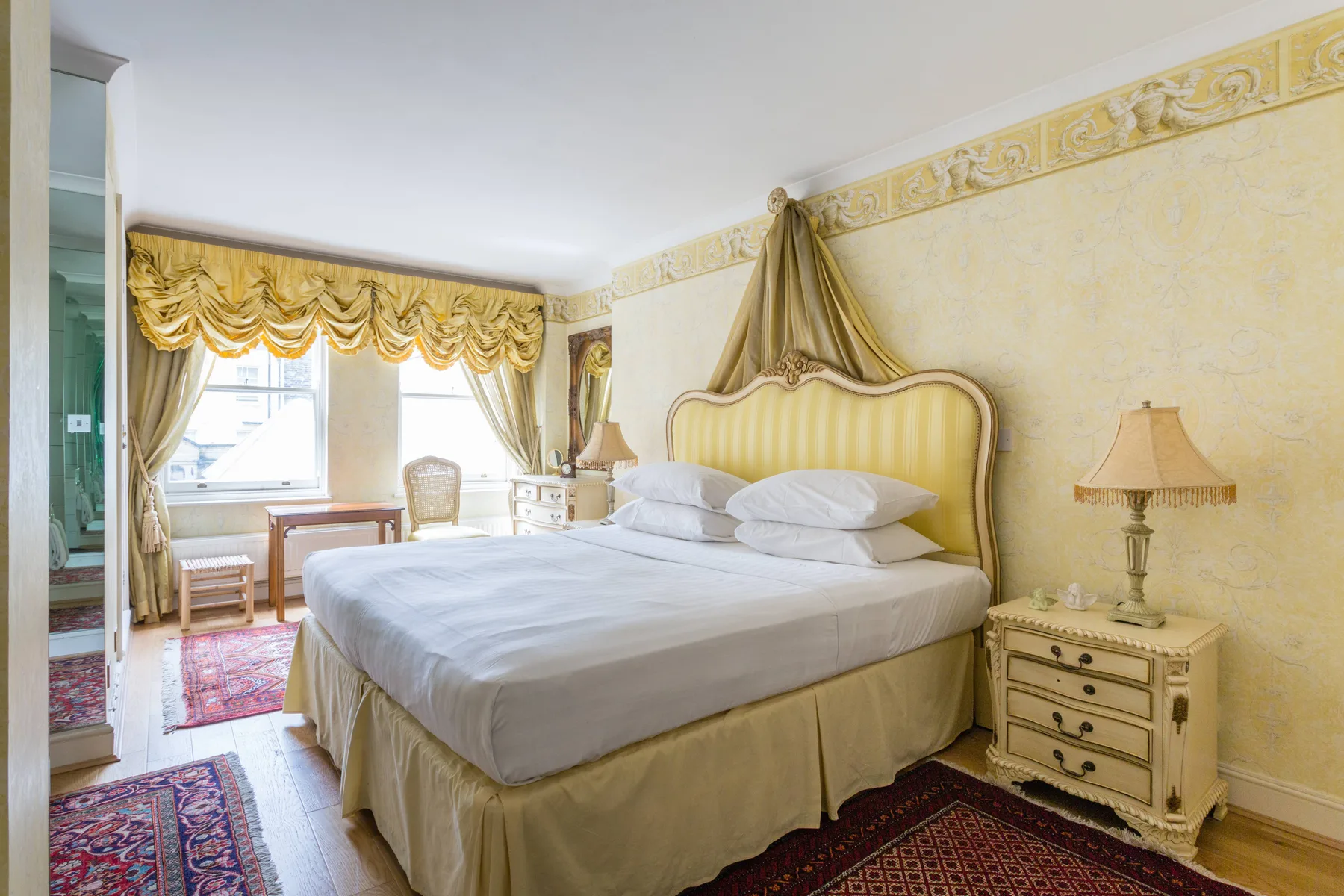 A bedroom with a large bed, decorative headboard, and window with draped curtains.