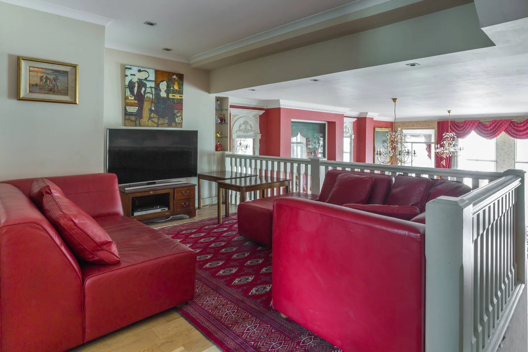 Una sala de estar con asientos rojos, un televisor y una alfombra estampada.