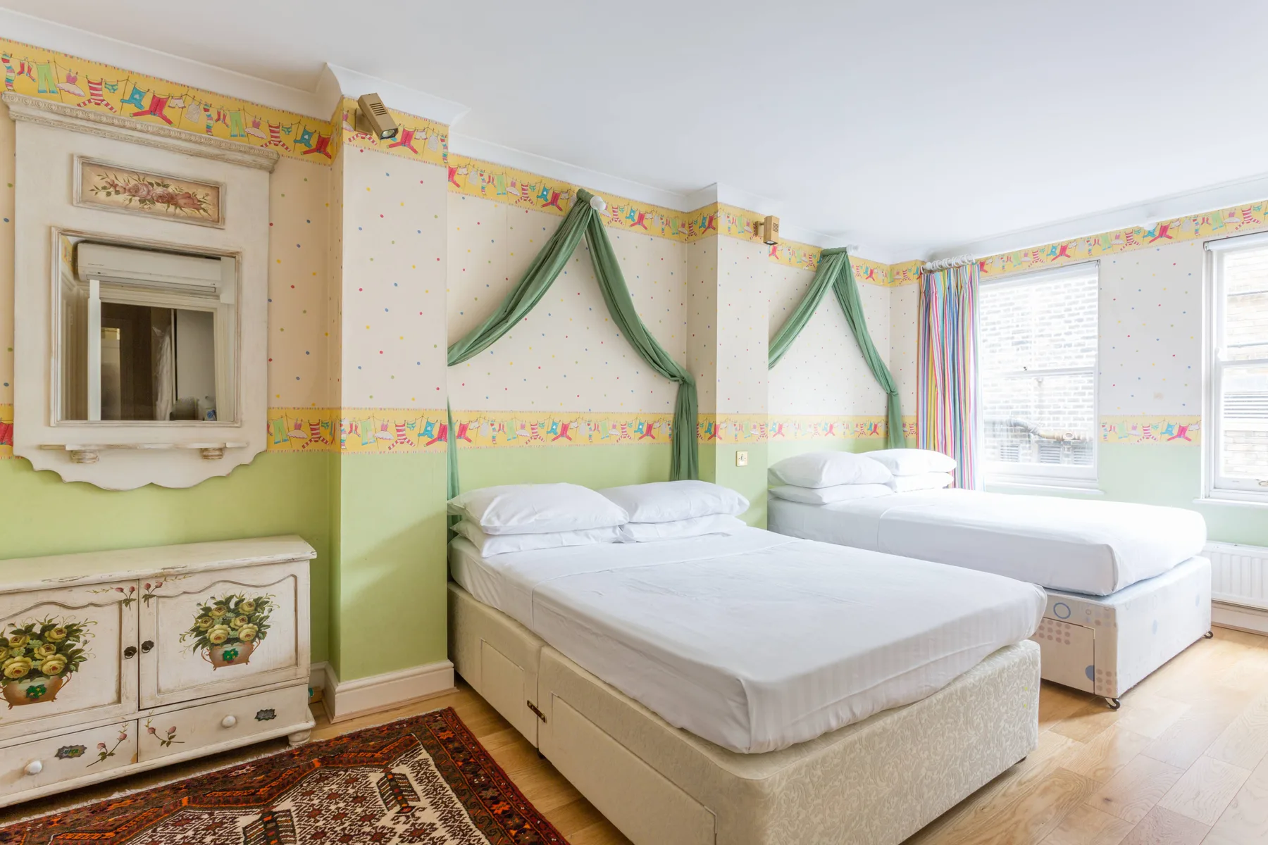 A bright bedroom with two beds, colorful wallpaper, and large windows.