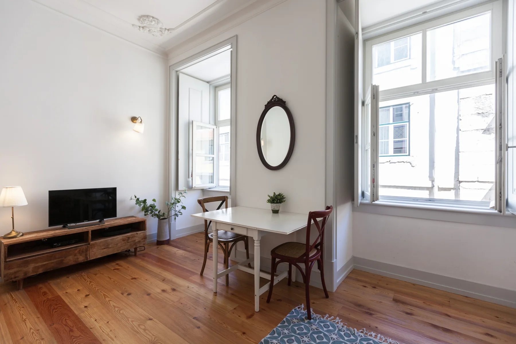 A bright dining area with a table beside tall windows and a television.
