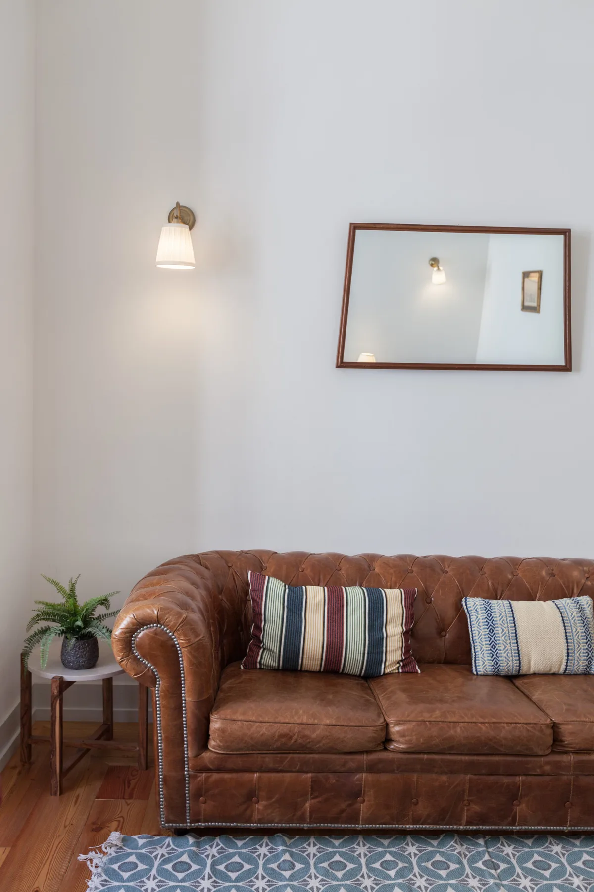 A living room features a brown sofa, wall mirror, and patterned rug.