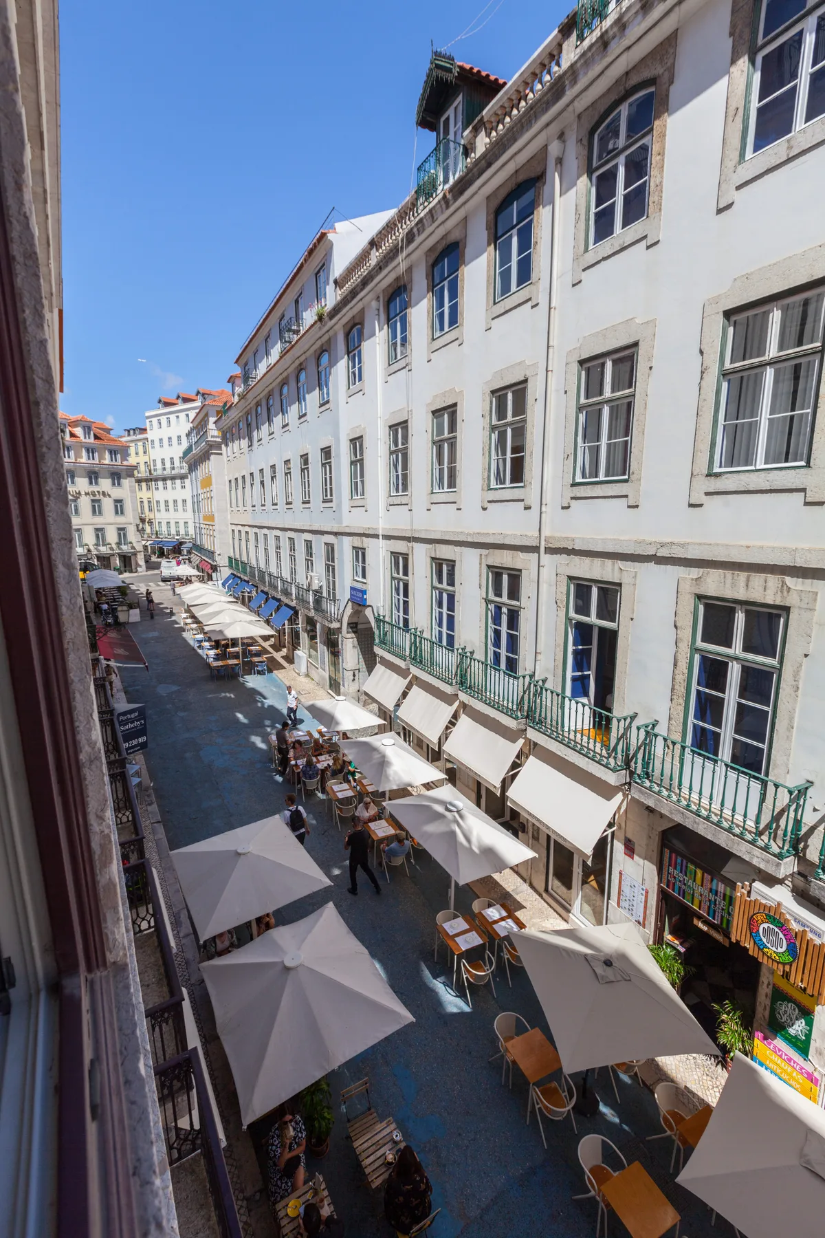 A narrow street lined with cafés, outdoor seating, and light-colored buildings.