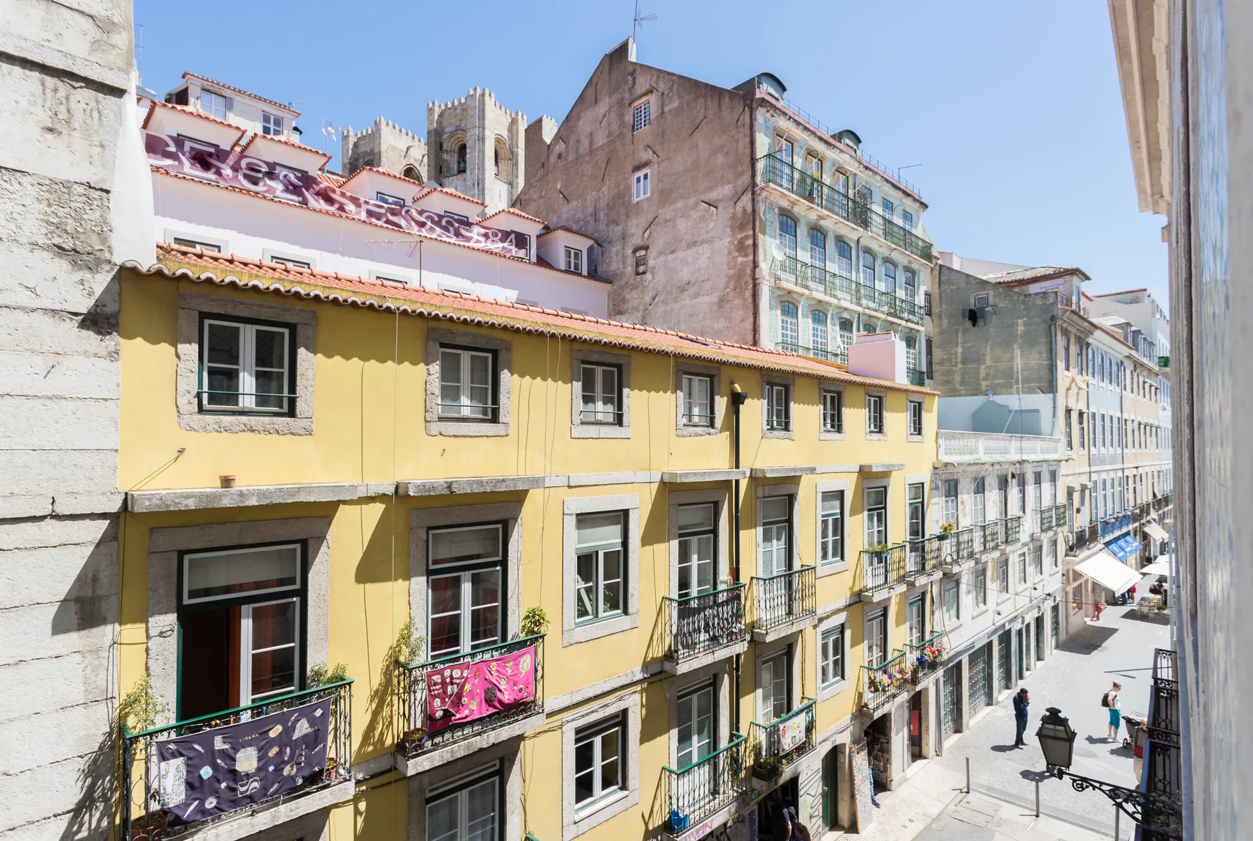 A sunny city street lined with colorful multi-story buildings and balconies.
