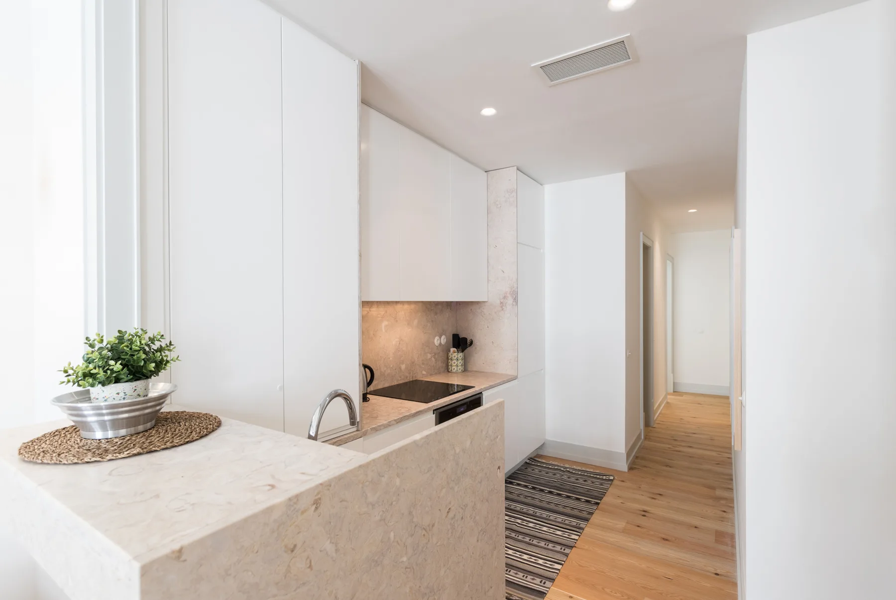 A bright kitchen opens onto a hallway with light wood flooring.
