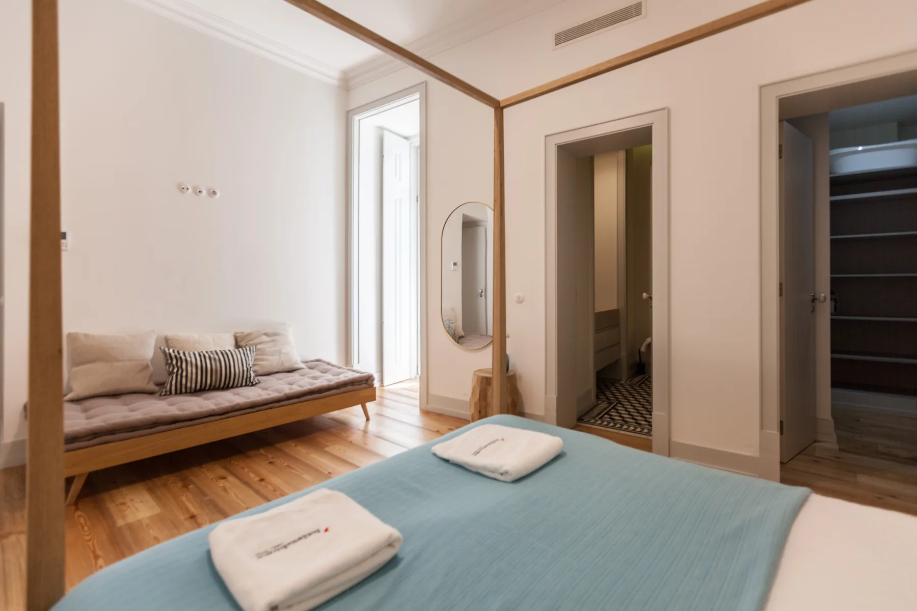 A bedroom with a low bed, folded towels, and a small seating area.