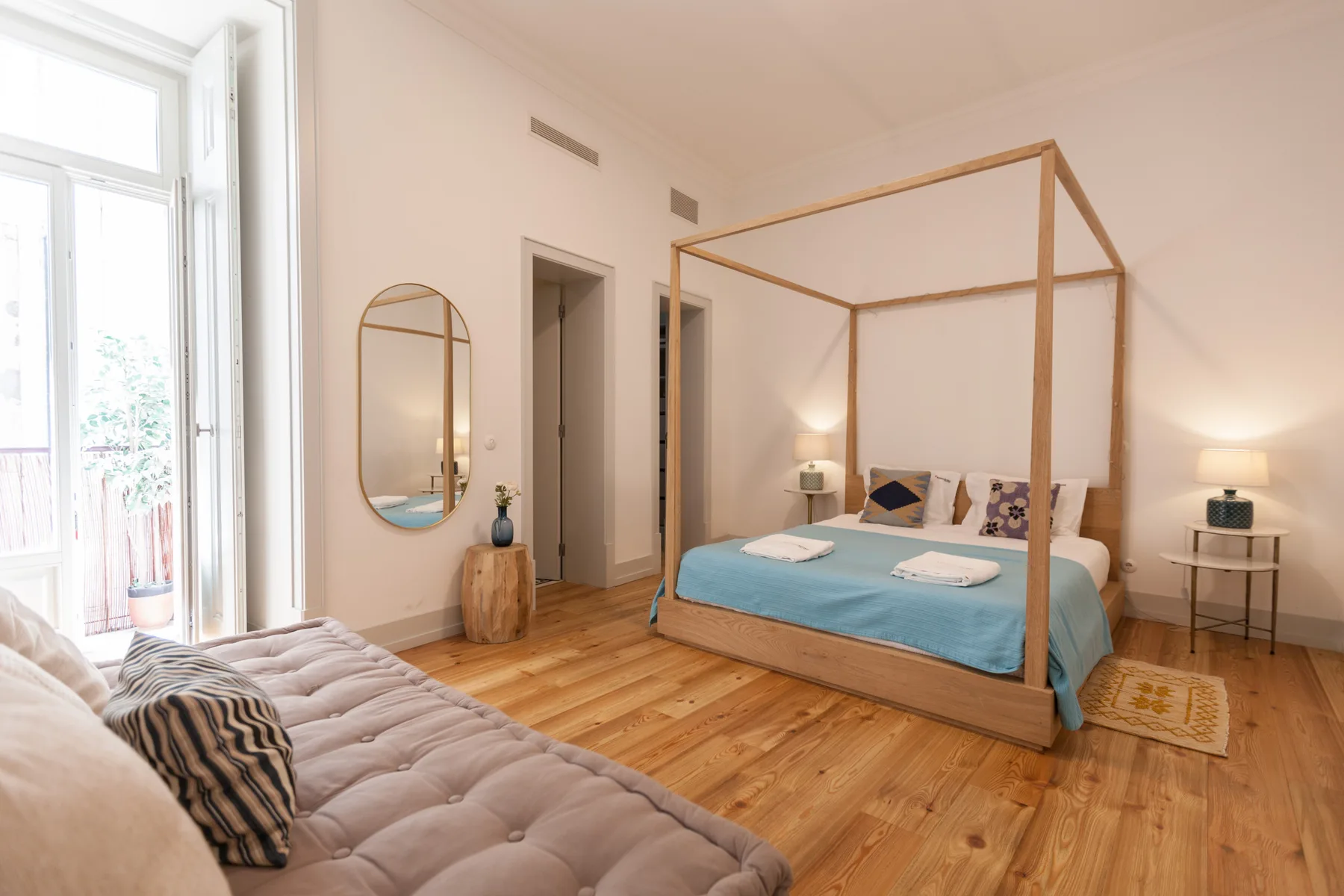 A bright bedroom with a canopy bed and a sofa beside the window.