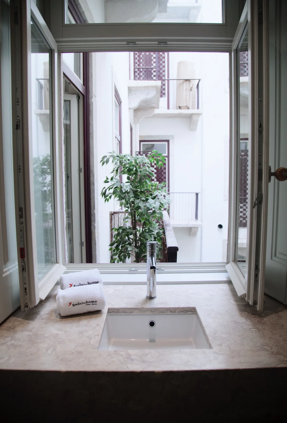 A bathroom sink sits beneath an open window overlooking a courtyard.