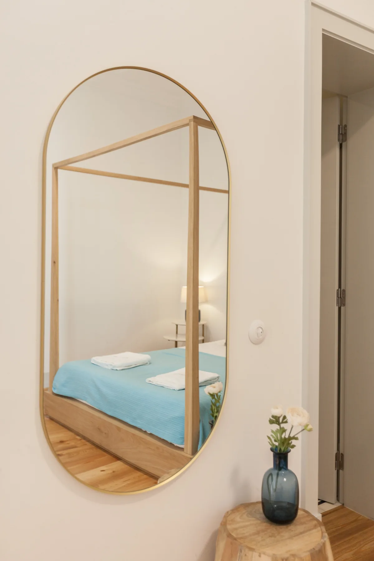 A bedroom with a turquoise bed reflected in a tall oval mirror.