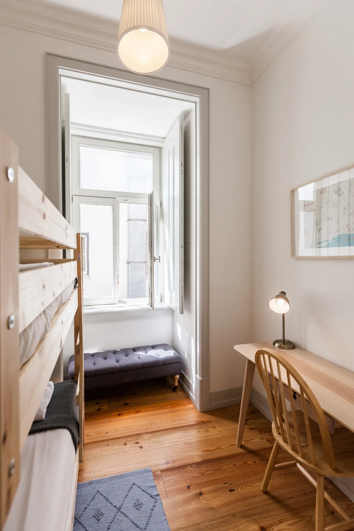 A bright bedroom with a bunk bed, desk, and window.