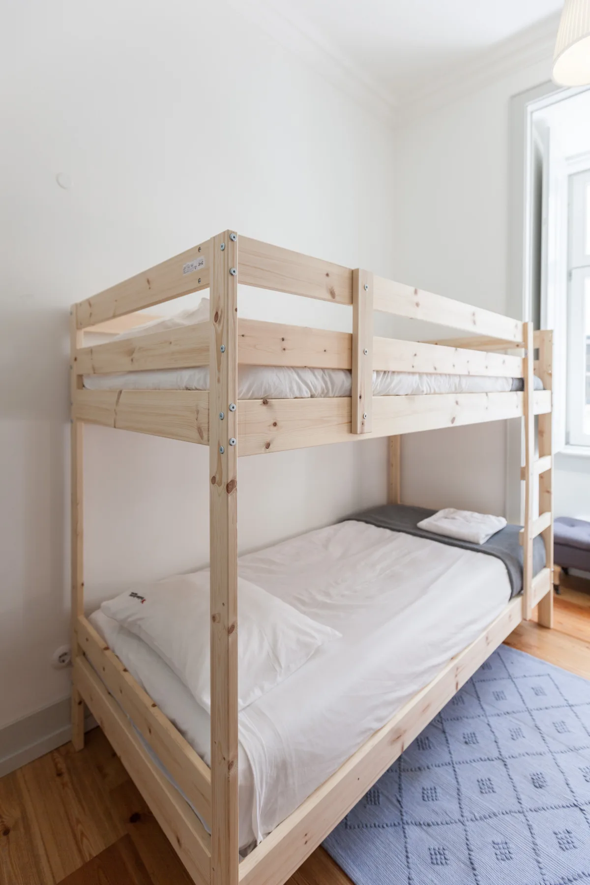 A bright bedroom with a wooden bunk bed and white bedding.