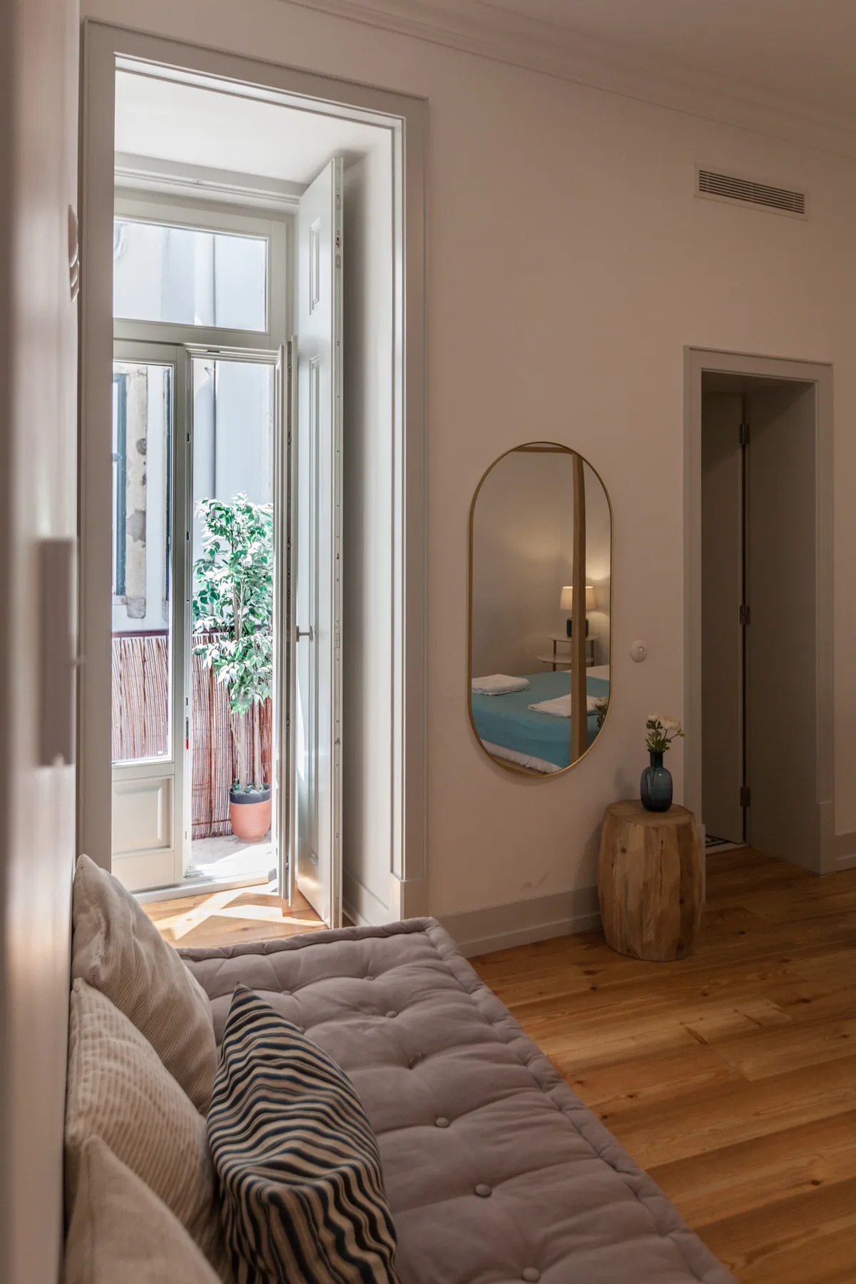A living room with a sofa, an oval mirror, and an open doorway to a balcony.
