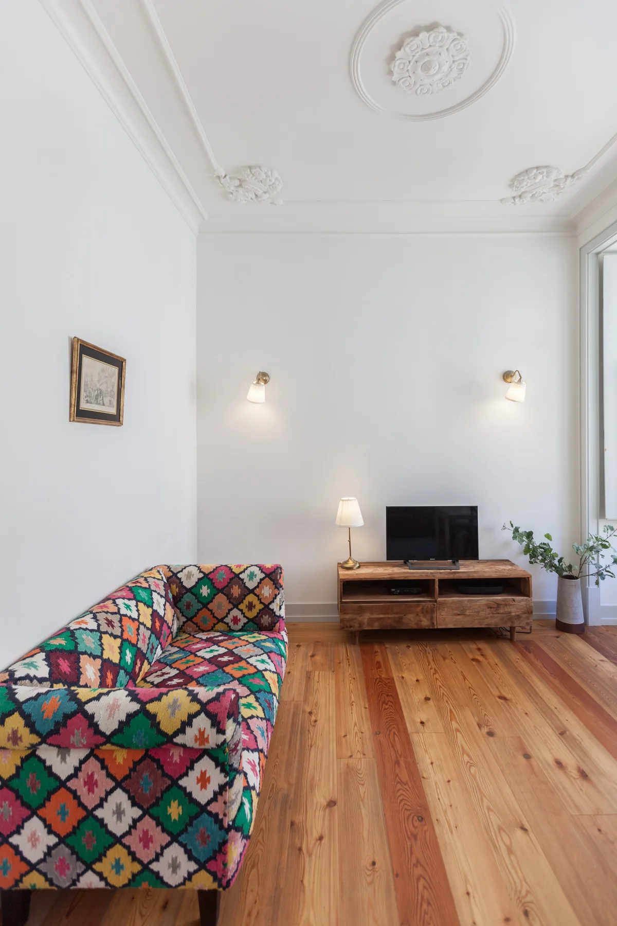 A living room with a patterned sofa, television, and wooden floor.