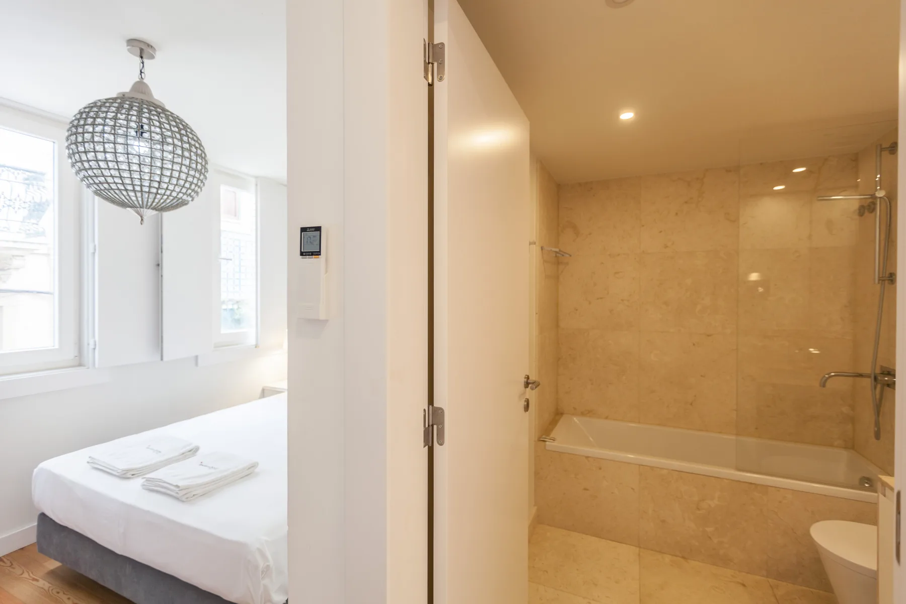 Dormitorio con una cama bien tendida junto a un baño con bañera.