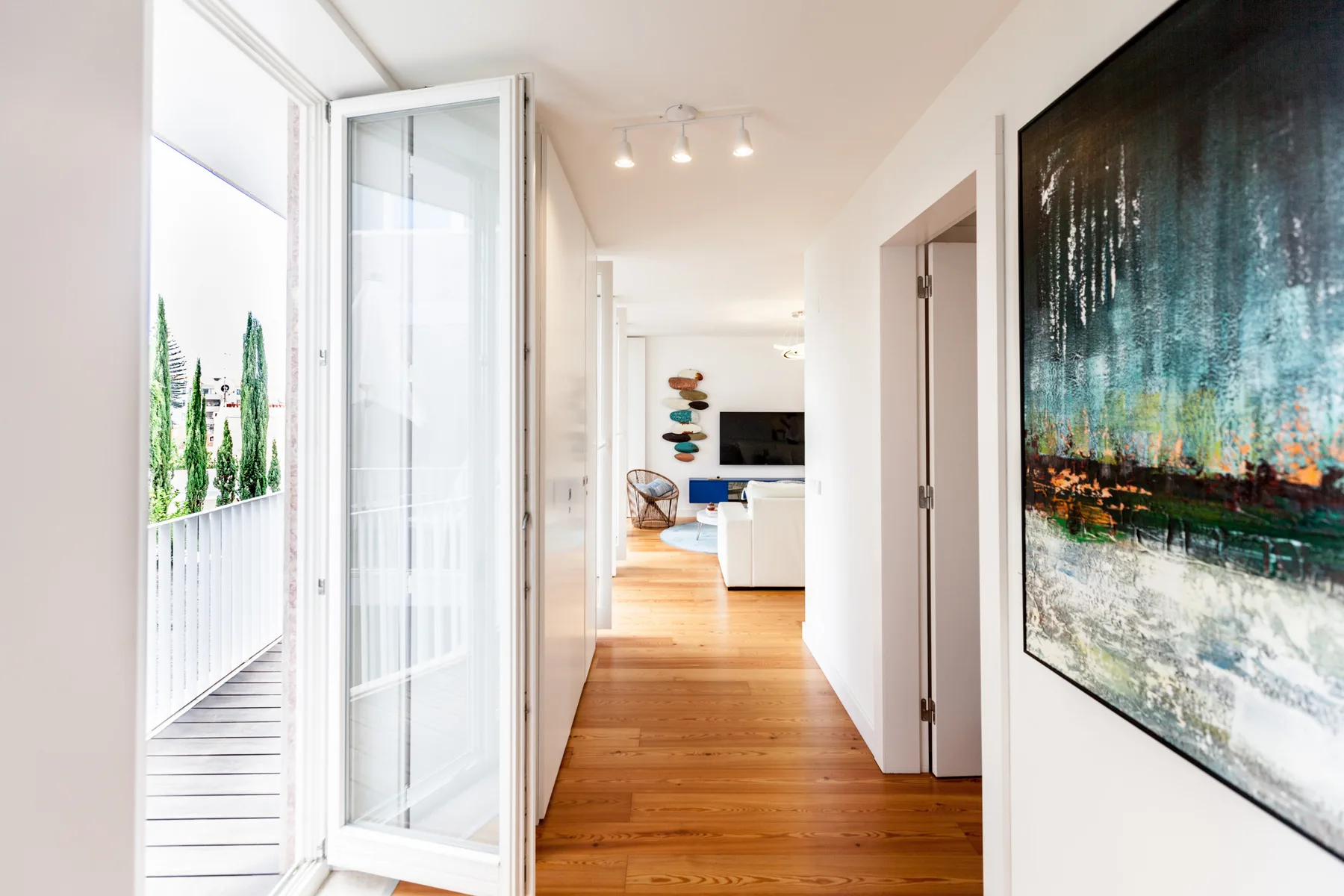 Un pasillo luminoso de apartamento da a una sala de estar, con una puerta de vidrio abierta.