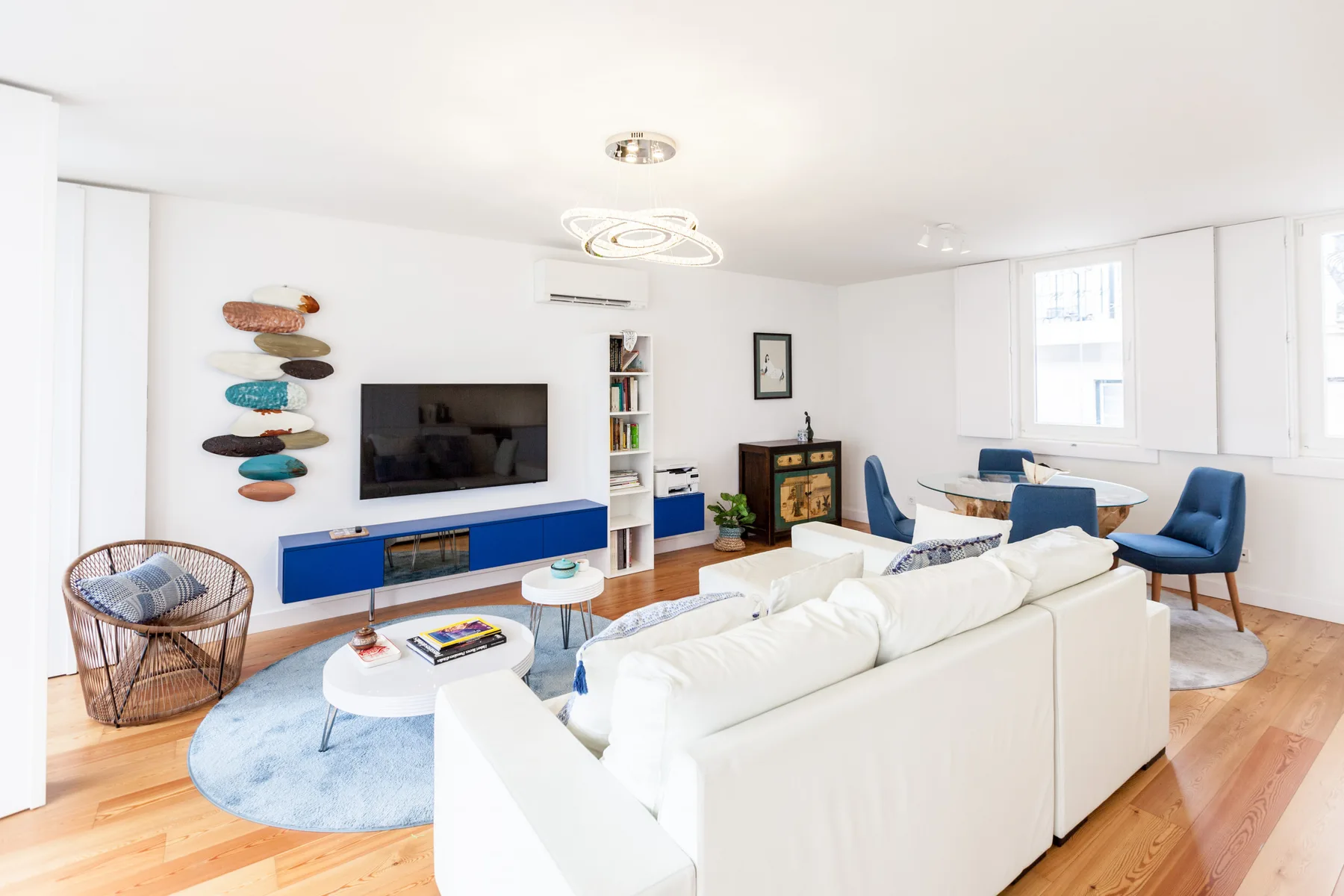 A bright living room with a white seating area, television, and large windows.