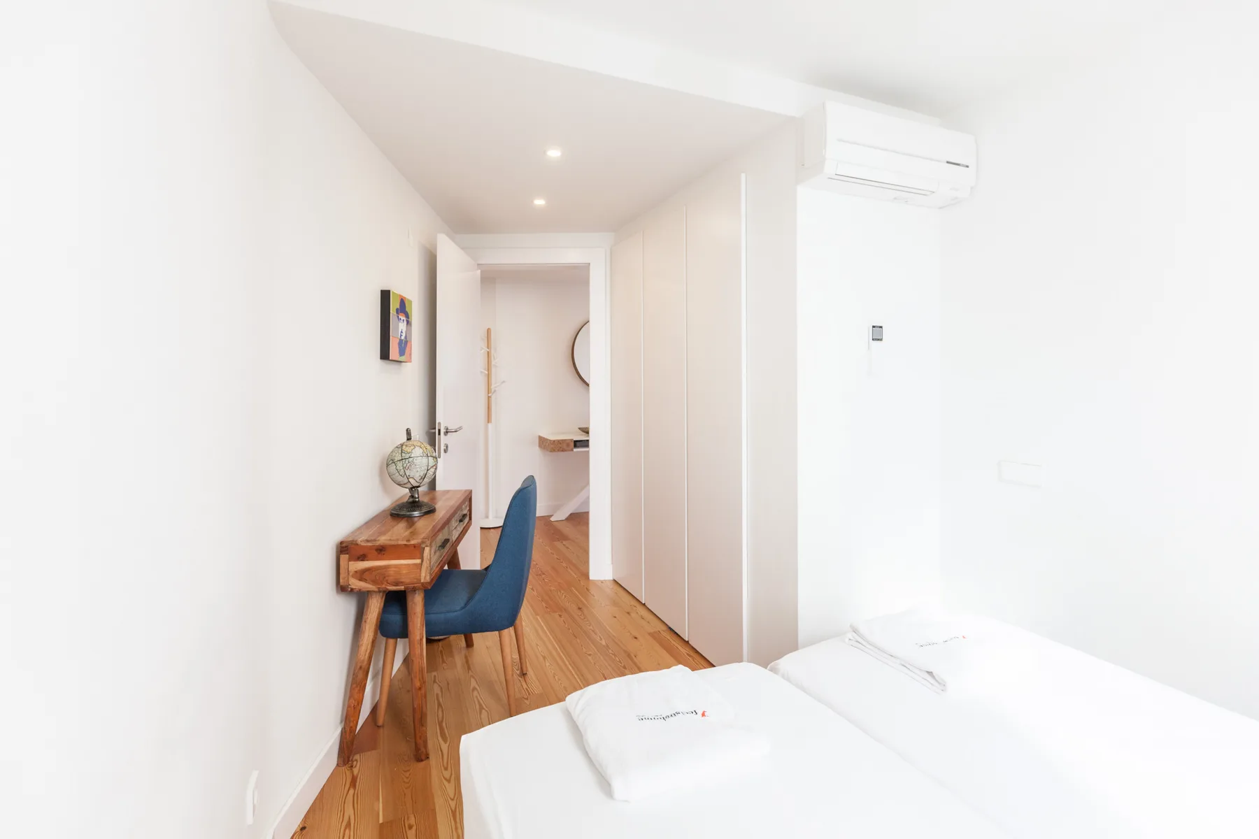 Un dormitorio luminoso con un escritorio y asiento azul junto a la cama.