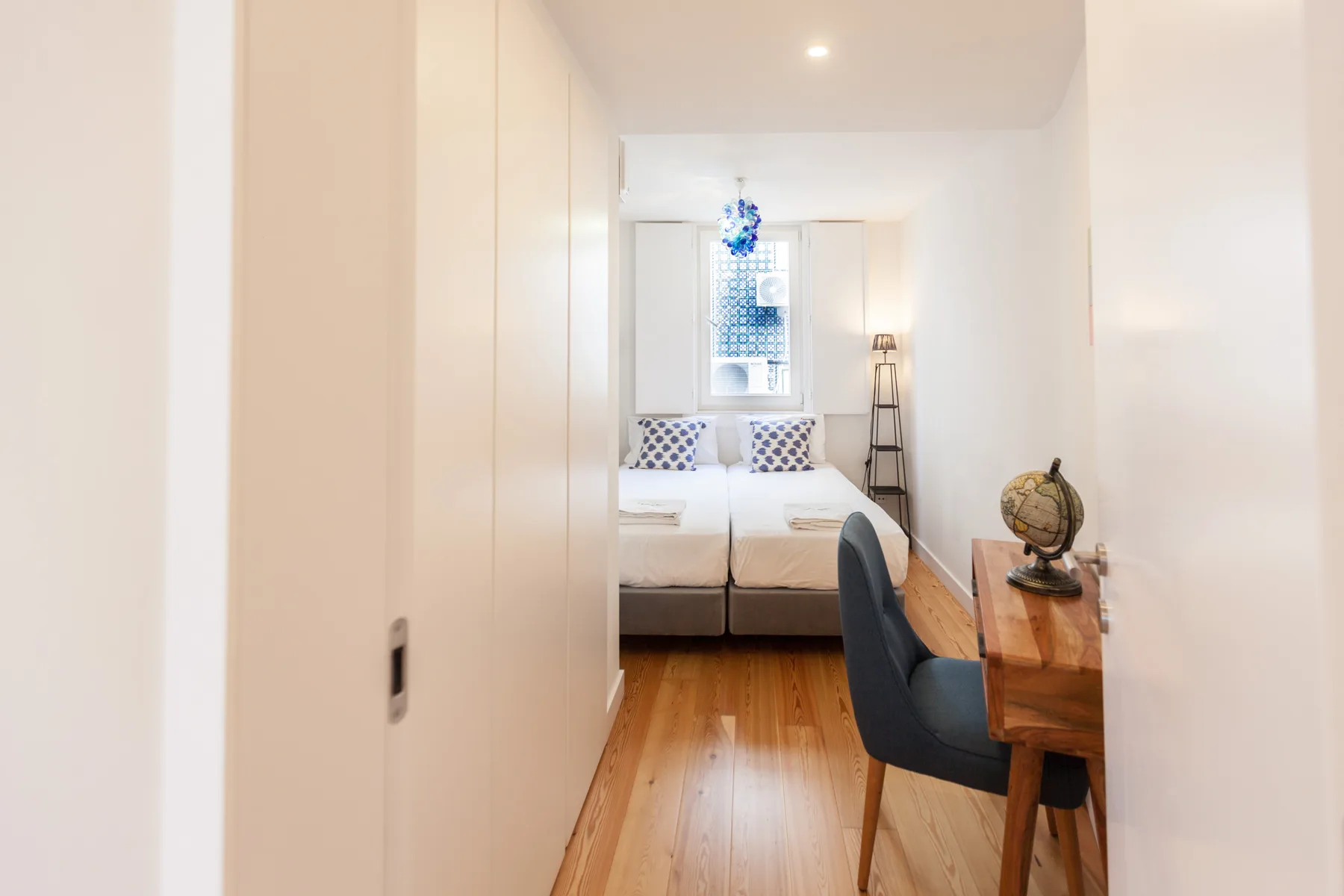 Un dormitorio luminoso con dos camas y un escritorio junto a la pared.